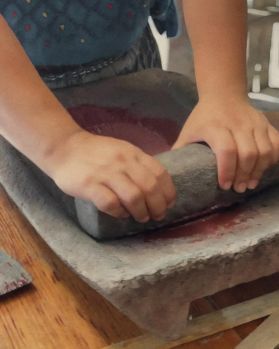 Two hands pressing a stone roller over cacao on a metate