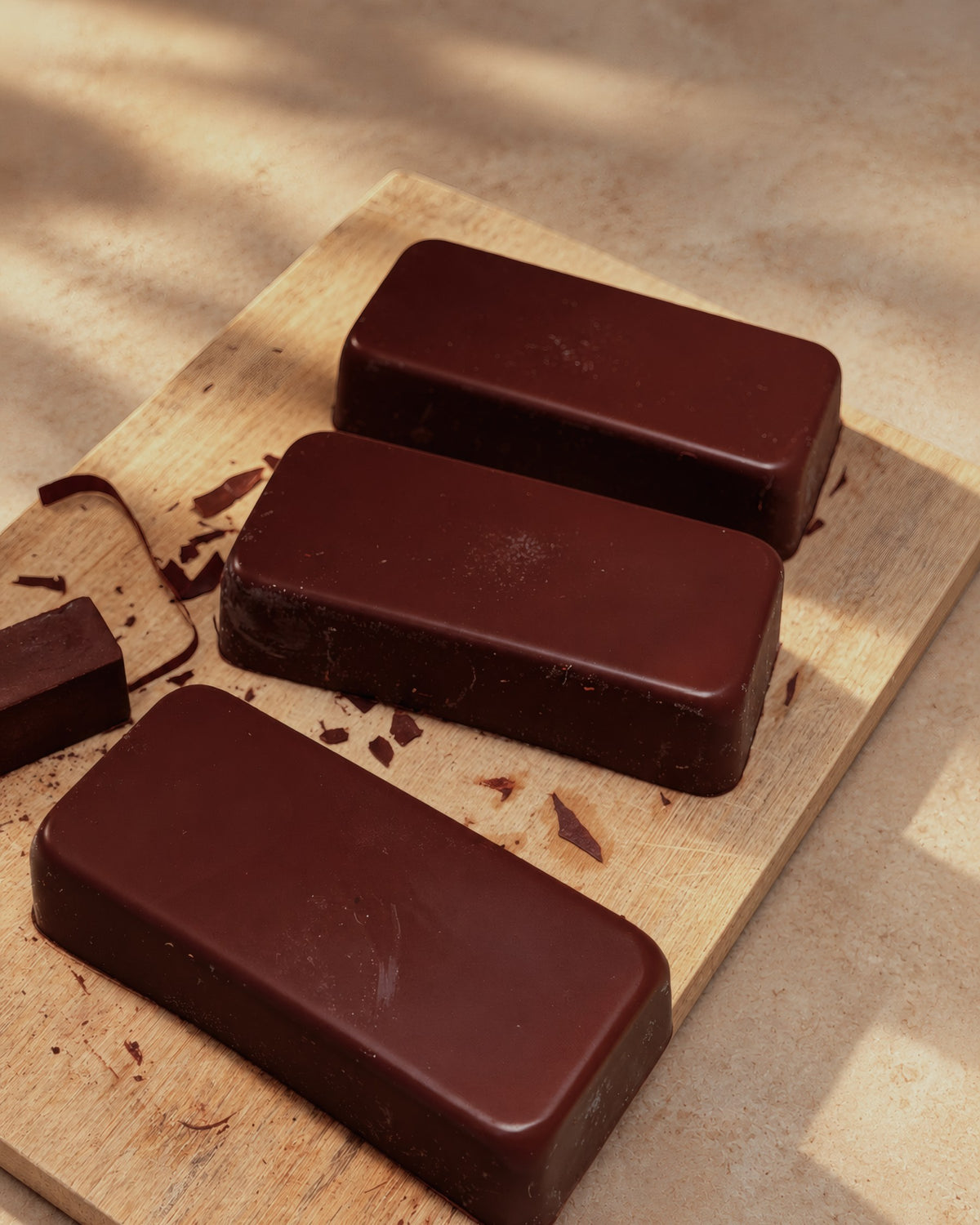 Three blocks of ALPAKA ceremonial cacao on a wooden board, with a few broken pieces